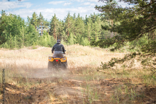 A man riding ATV on a sand road in a forest, back view