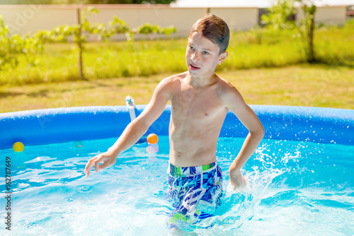 Adorable young boy enjoying and cooling in backyard pool on hot summer day