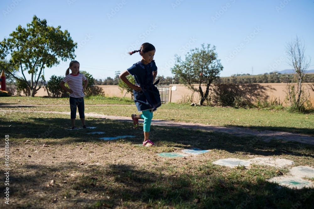 Playful friends with hands on hip jumping on grassy field 