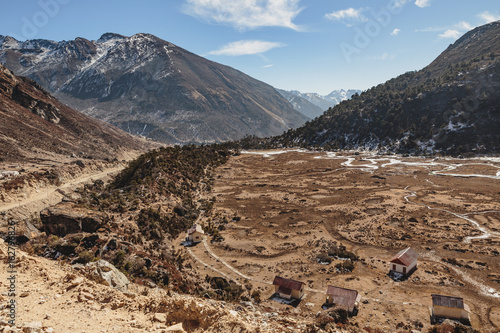 Black mountain with snow on the top and brown mountain with Houses and glacial traces on yellow stone ground at Thangu and Chopta valley in winter in Lachen. North Sikkim, India. photo