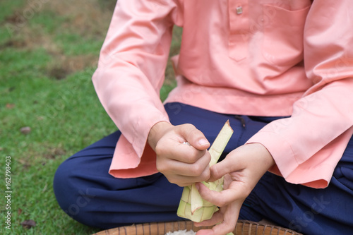 The boy is filling the rice into the ketupat clad