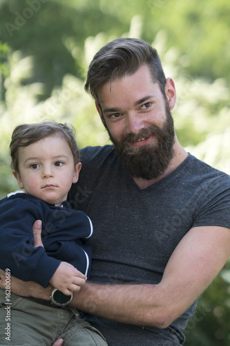 Young bearded hipster father holding his little son in park © cineberg