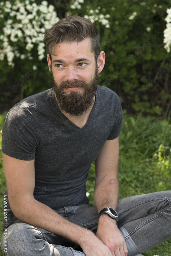 Young hipster with beard sitting with crossed legs in park Young hipster with beard sitting with crossed legs in park
