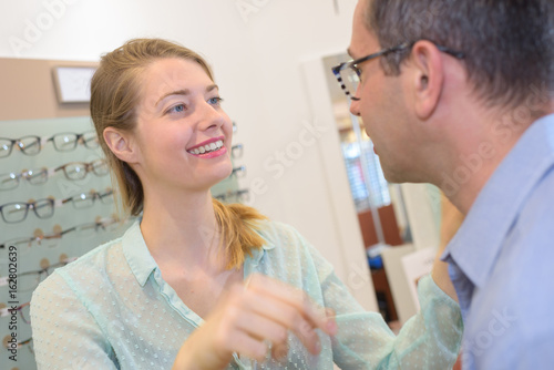 optician showing glasses to man at optics store