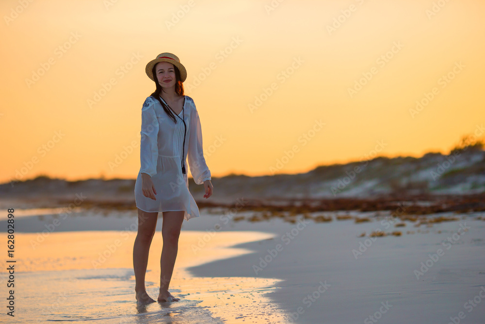 Young beautiful woman on tropical seashore in sunset. Happy girl in dress in the evening on the beach Young beautiful woman on tropical seashore in sunset. Happy girl in dress in the evening on the beach