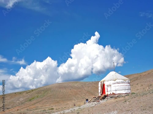 Clouds flying in a deep blue sky with ethnic yurts and mountains in background