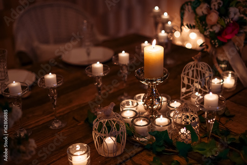 Candles in the flasks set on table decorations surrounding plates at cozy warm atmosphere