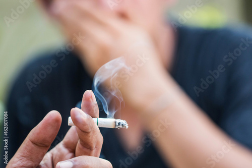 Passive smoking concept. Man is smoking cigarette and man is covering face. A lot of smoke around.
