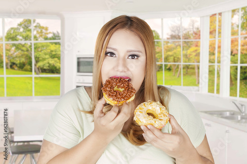 Obese woman eats two donuts at home