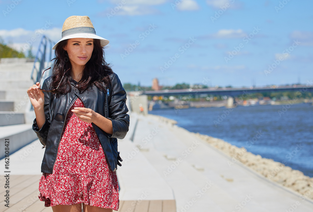 Expressive attentive look woman in grey  hat. Urban port river background. Natural sunset light