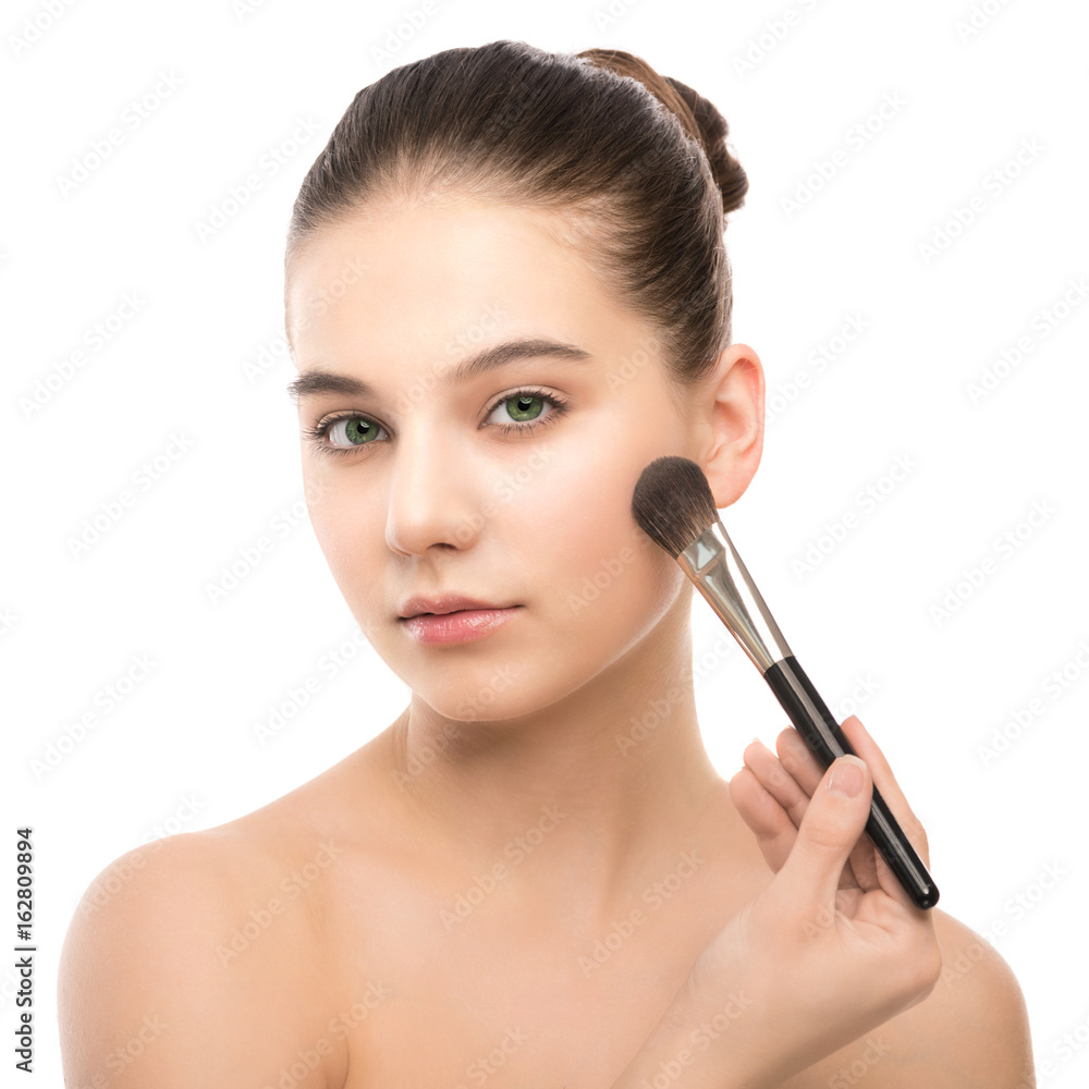 Portrait of beautiful young brunette woman with clean face. Beauty spa model girl with perfect fresh clean skin applying cosmetic brush. Youth and skin care concept. Isolated on a white background.