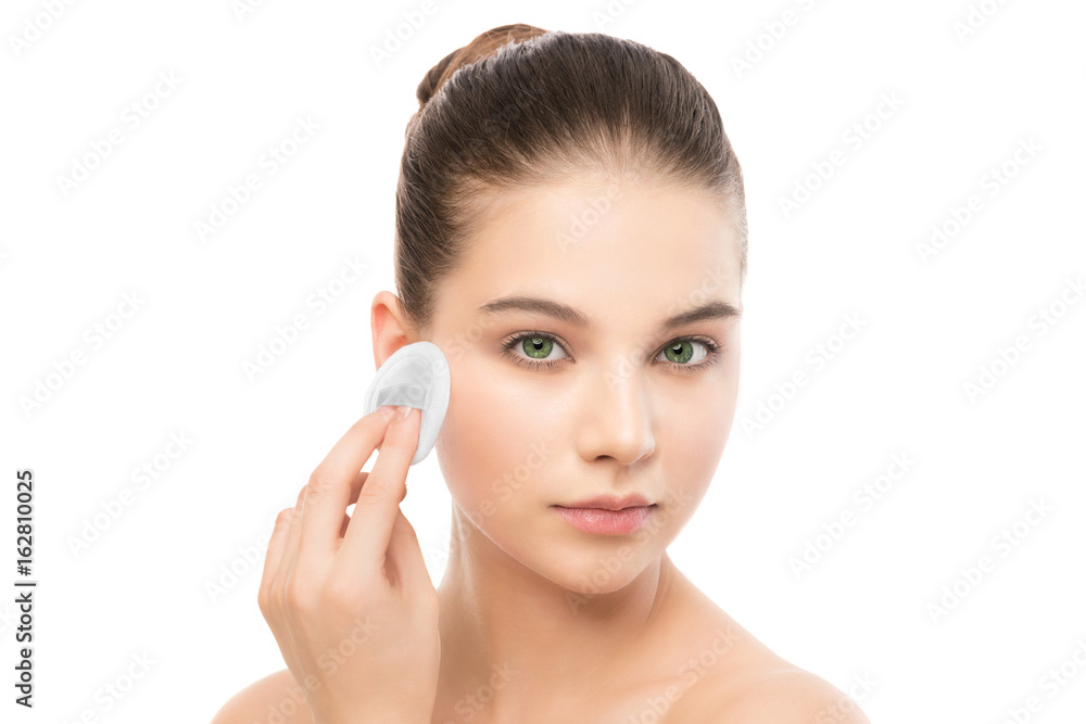 Young girl cares for face skin relaxation. Beautiful young brunette woman with clean perfect fresh skin using cotton pad. Youth and skin care concept. Isolated on a white.