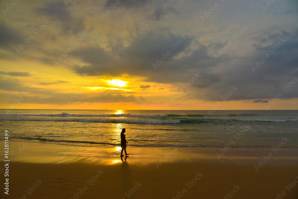 Silhouette woman walking along the beach at sunset.