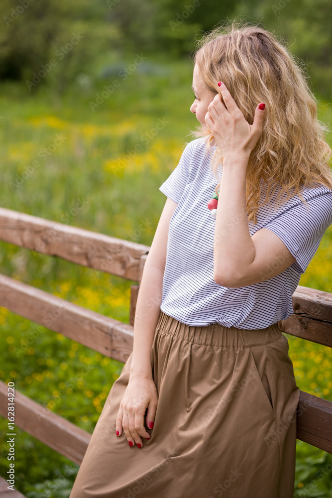 Portrait of young blond woman standing near wooden fence in the park on a sunny summer day. Lifestyle. Outdoor. Portrait of young blond woman standing near wooden fence in the park on a sunny summer day. Lifestyle. Outdoor.