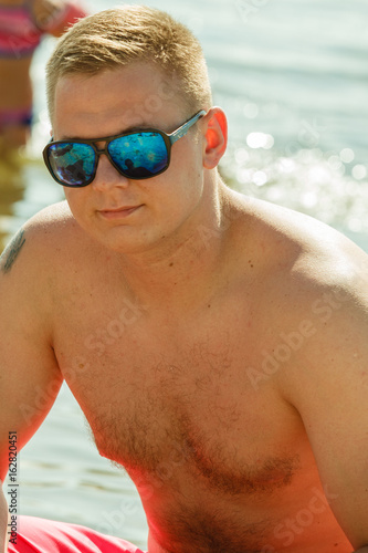 Man in sunglasses crouching near sea © Voyagerix