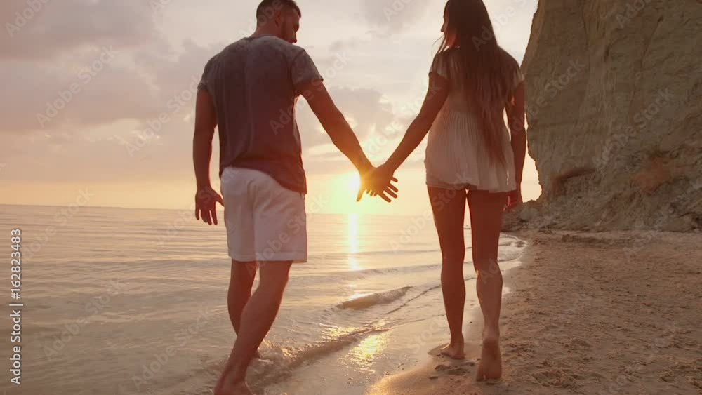 Couple Walking Along Summer Beach at Sunset Couple Walking Along Summer Beach at Sunset