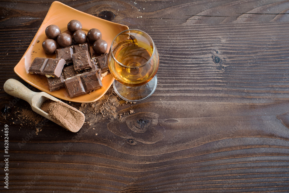 A glass of brandy. Whiskey. Assortment of chocolates on the wooden surface. Top view. A glass of brandy. Whiskey. Assortment of chocolates on the wooden surface. Top view.