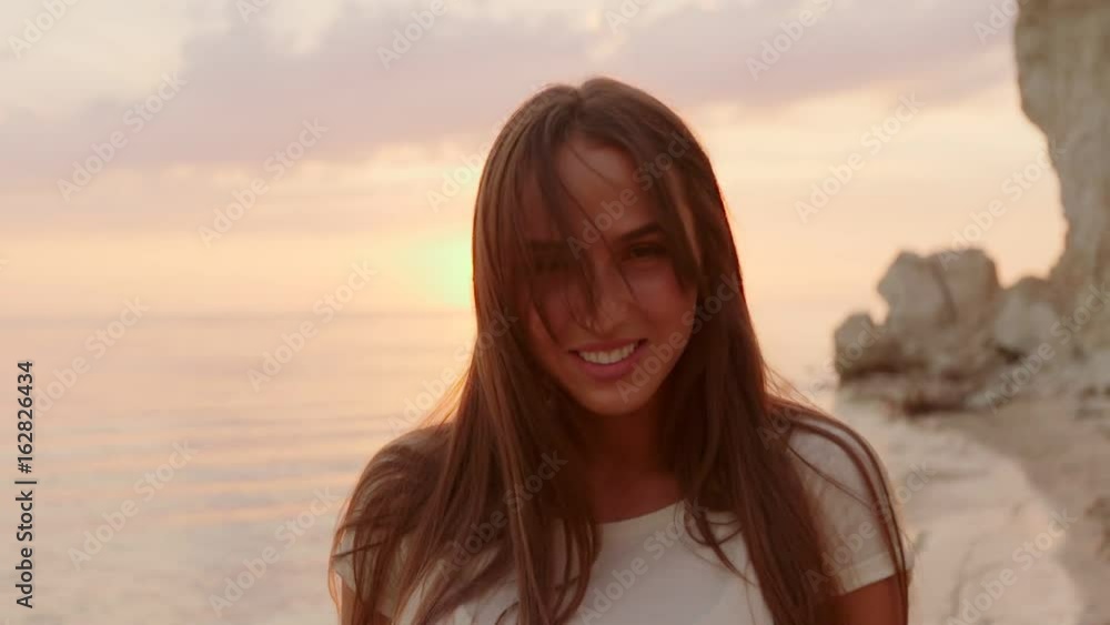 Close up portrait of beautiful young woman running hand through hair blowing in wind on tropical beach slow motion Close up portrait of beautiful young woman running hand through hair blowing in wind on tropical beach slow motion