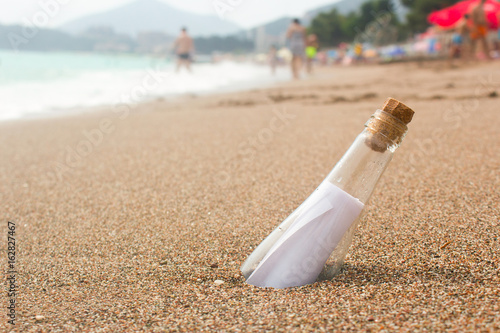 Message in a glass bottle on the beach. People bathe in the sea on the waves. Found a note on salvation, please help
