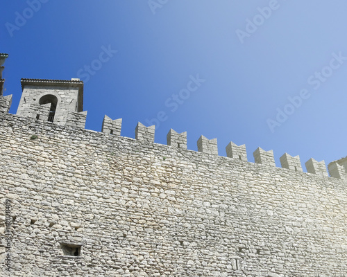фрагмент каменной стены старинной крепости в Италии на фоне голубого неба 