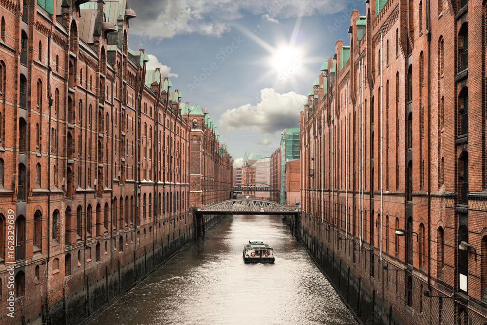 boat on a channel in the old warehouse district Speicherstadt in Hamburg, Germany under sunny blue sky