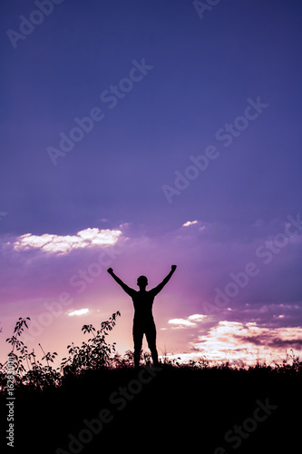Silhouette of a man with raised-up arms at the beautiful sunset on the mountain on a purple background sky