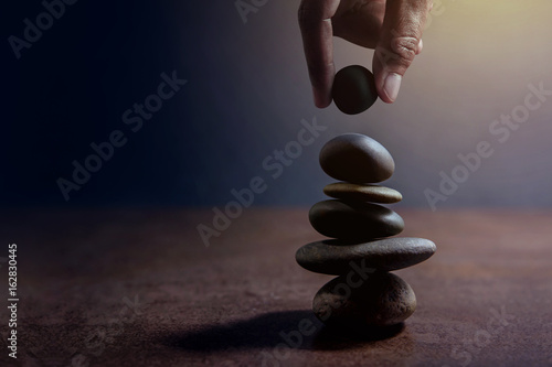 Balance concept between of Life and work present by Hand setting a natural zen rock stone on Stack, Side view and Dark light