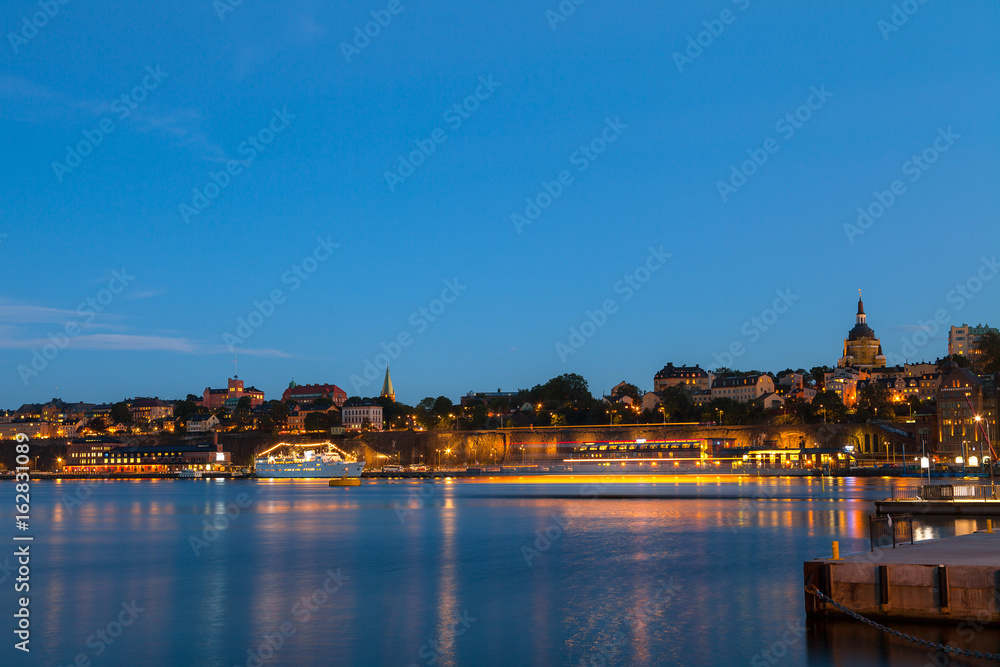 Fototapeta premium Nocny widok Sztokholmu. Podświetlane łodzie wzdłuż nabrzeża miasta.