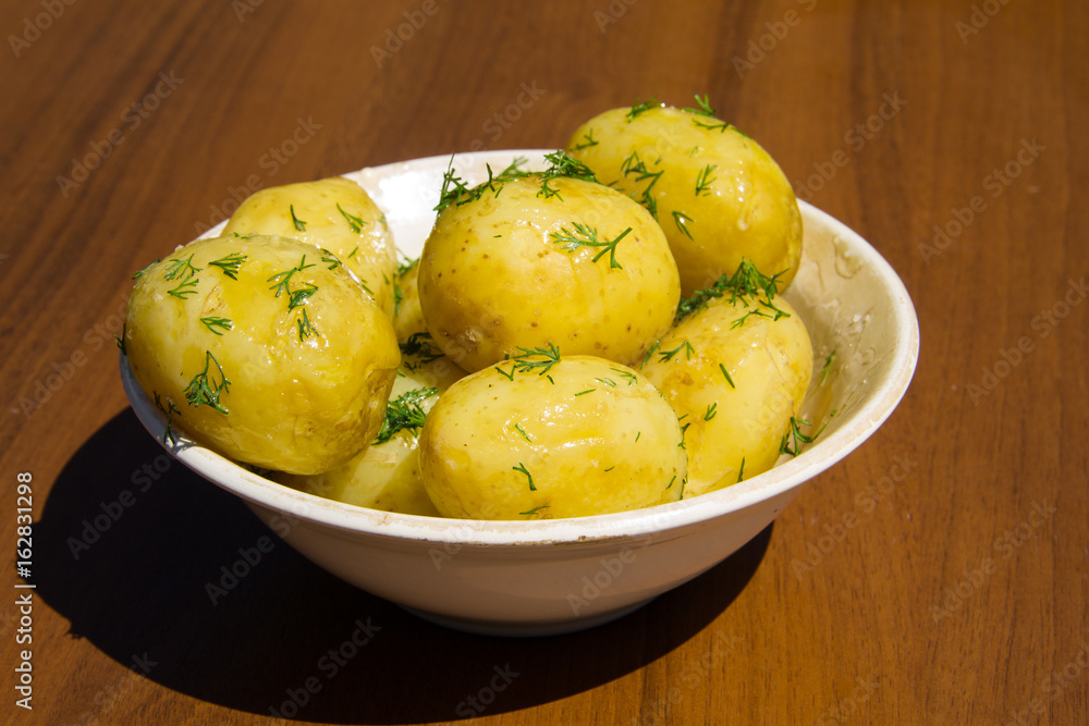 Boiled new potatoes with butter and dill on wooden table