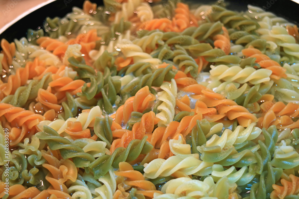 Three-color spiral shaped pasta (fusilli) being boiled in a frying pan Three-color spiral shaped pasta (fusilli) being boiled in a frying pan