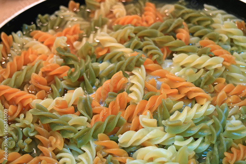 Three-color spiral shaped pasta (fusilli) being boiled in a frying pan 