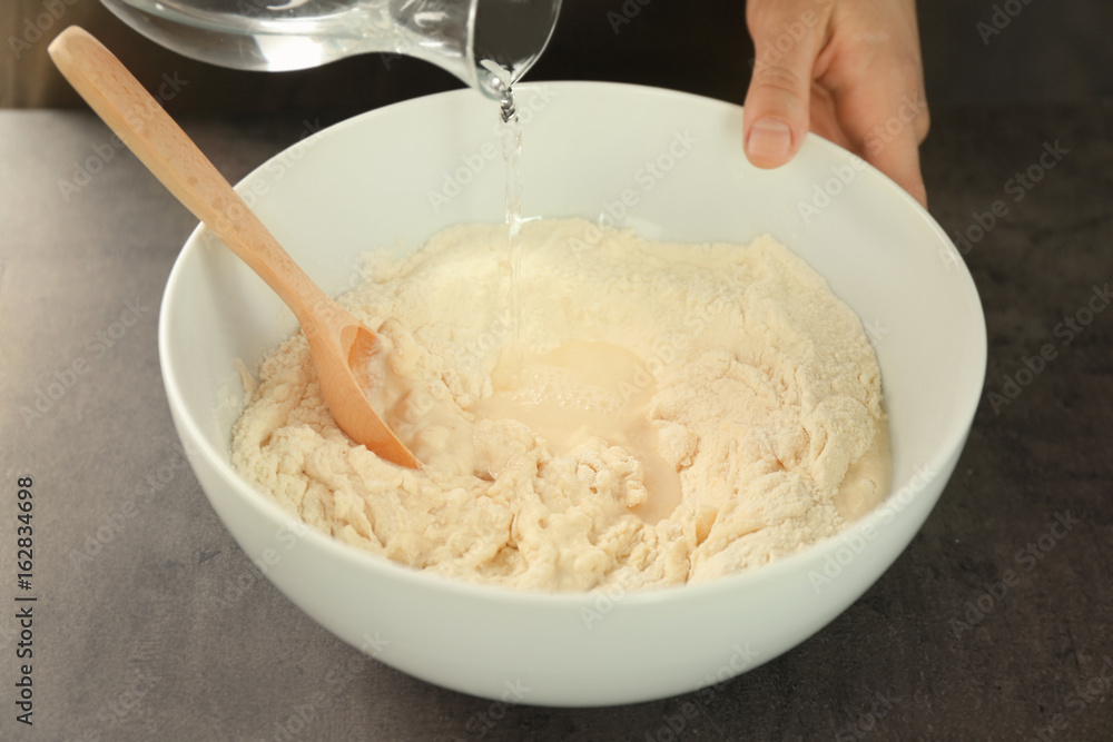 Chef pouring water into glass bowl with flour on table Chef pouring water into glass bowl with flour on table