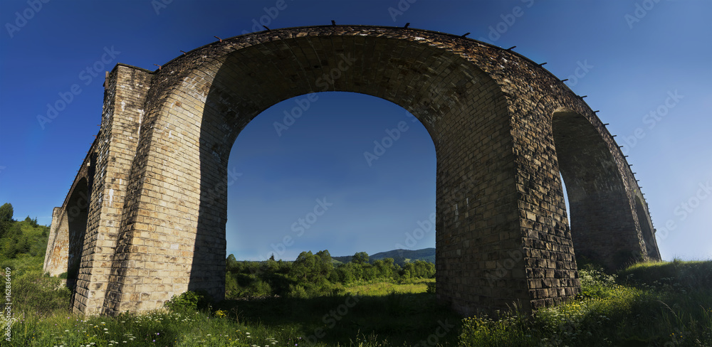 Panorama of an old arched stone bridge in a mountain valley