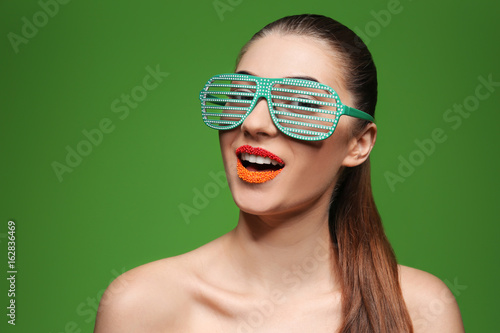 Portrait of beautiful woman with creative makeup and party glasses on color background
