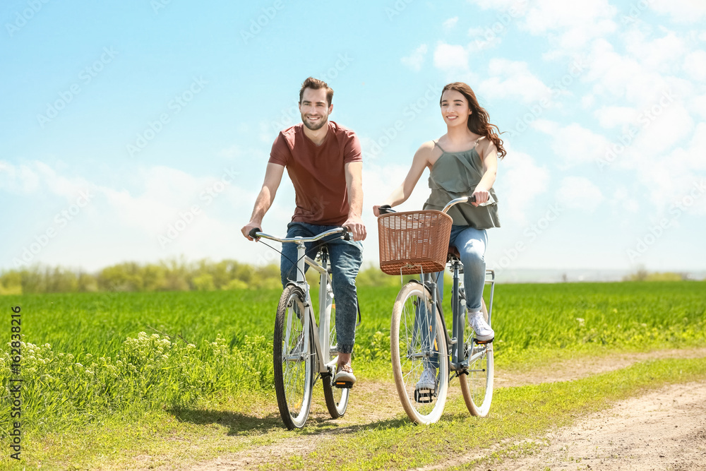 Happy young couple riding bicycles in countryside