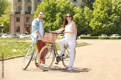 Happy young couple with bicycles in park on sunny day