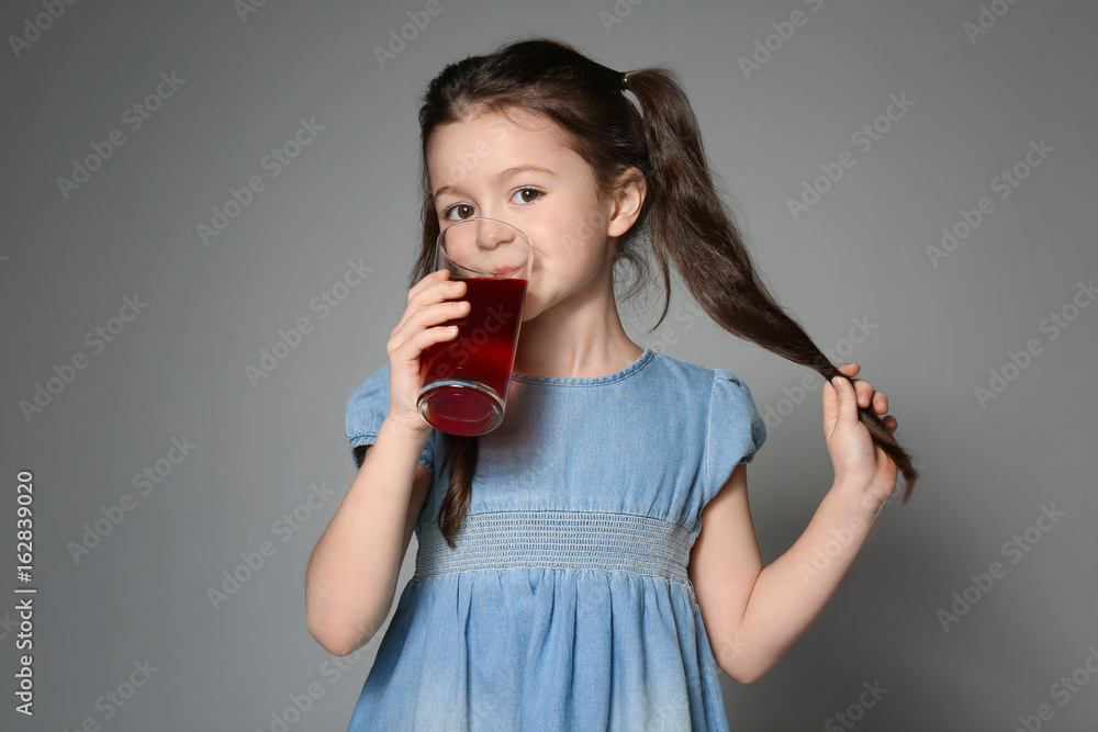 Cute little girl drinking juice on grey background Cute little girl drinking juice on grey background