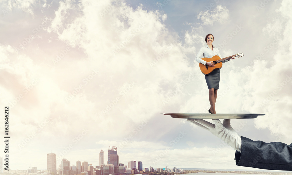Attractive businesswoman on metal tray playing acoustic guitar against cityscape background Attractive businesswoman on metal tray playing acoustic guitar against cityscape background