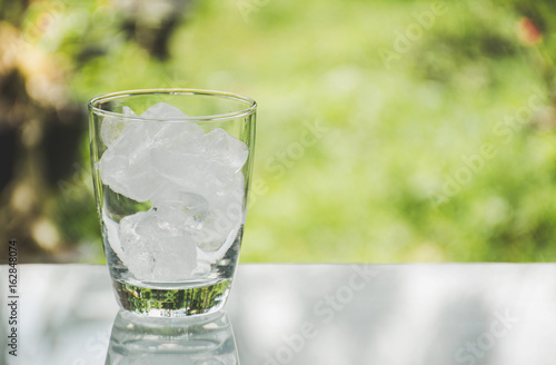 Ice cube in the glass on table with nature background