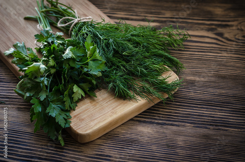 Parsley and dill on a cutting board, wooden background photo