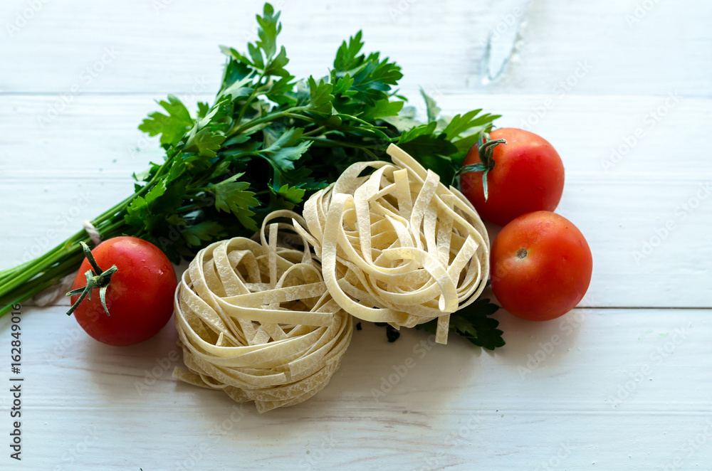 Tagliatelle with ingredients for cooking pasta. Curly parsley, garlic, tomatoes on a wooden table.
