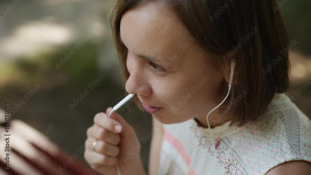 Lovely young woman talking with headphones and tablet in summer park. Lovely young woman talking with headphones and tablet in summer park.