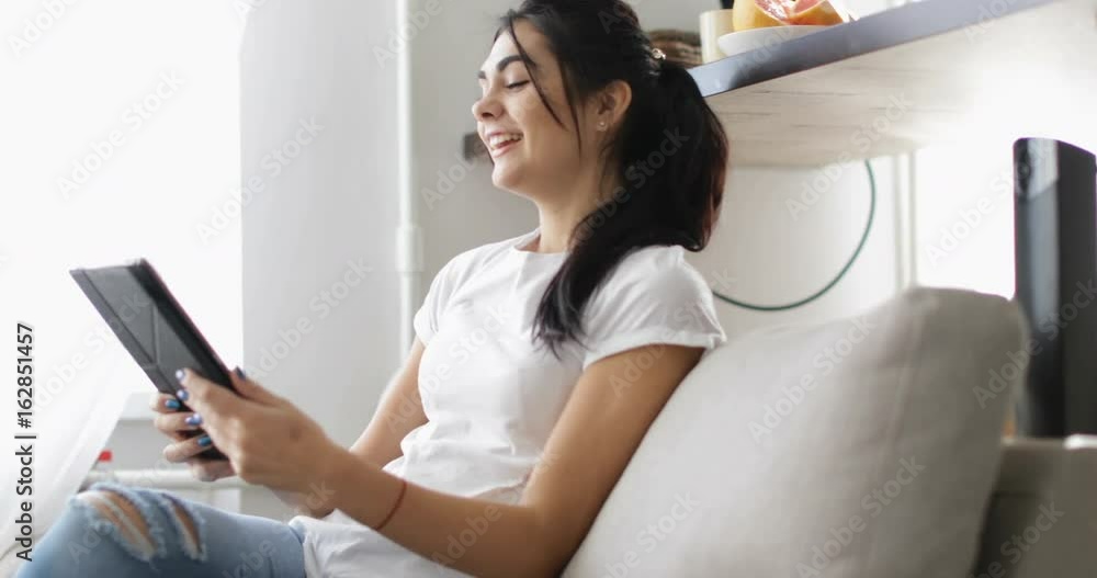 Young Woman Use Tablet Computer Sitting On Coach At Home, Happy Smiling Beautiful Girl Browsing Internet Online Slow Motion 60 Young Woman Use Tablet Computer Sitting On Coach At Home, Happy Smiling Beautiful Girl Browsing Internet Online Slow Motion 60