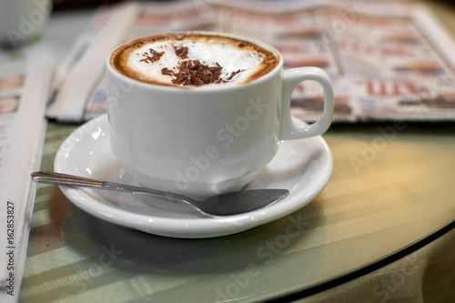 Selective focus on cappuccino on table at a cafe, surrounded by newspapers - coffee time the old way