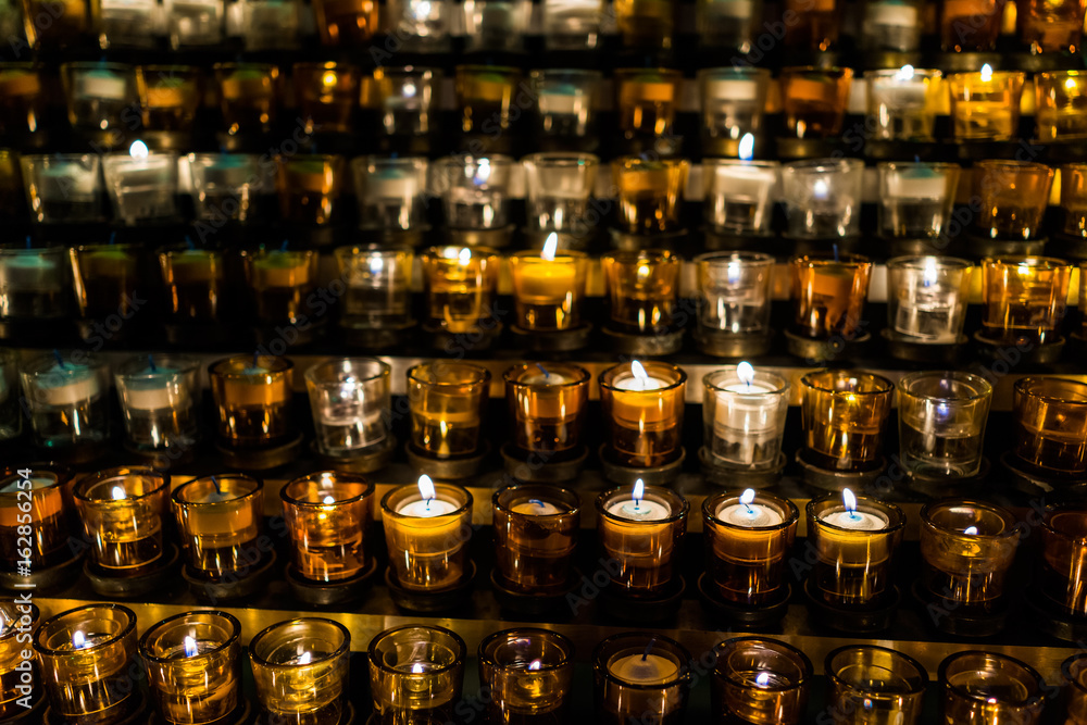Macro closeup of many yellow candles with flame in church