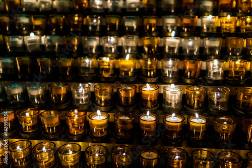Macro closeup of many yellow candles with flame in church