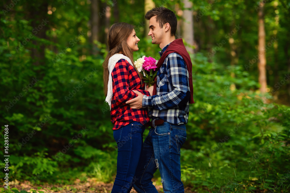 Stylish young couple in shirts and jeans while walking in the forest. A charming girl and her handsome boyfriend are looking at each other.