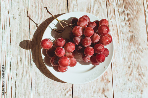 Fresh red grapes in a plate on wooden table, flatlay photo