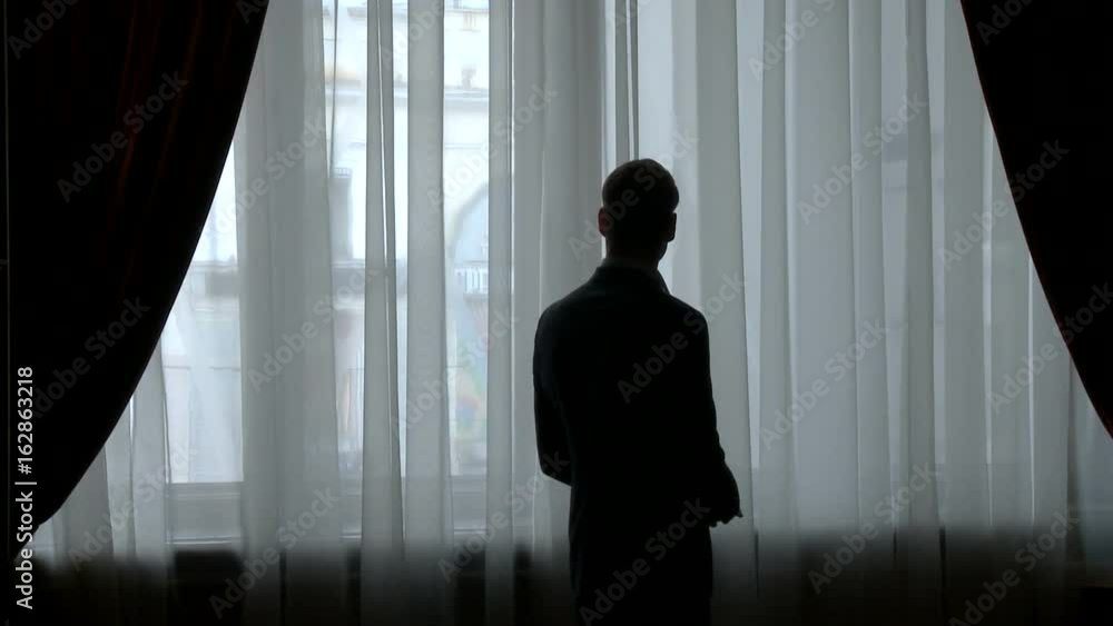 Young man, businessman wearing glasses, standing by the big window Young man, businessman wearing glasses, standing by the big window