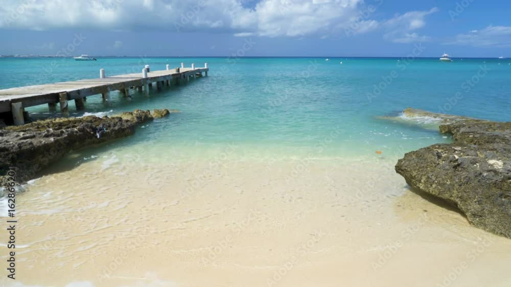 Caribbean beach background with turquoise water, dock, Grand Cayman island and boats in the background. Caribbean beach background with turquoise water, dock, Grand Cayman island and boats in the background.
